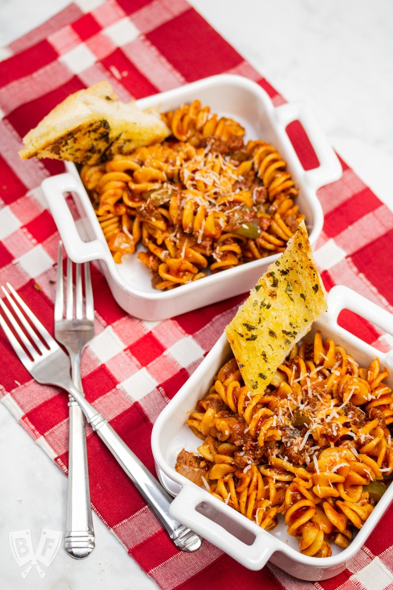 Overhead view of dishes of Instant Pot Tomato Beef Pasta with serving dishes with Parmesan cheese and garlic bread.