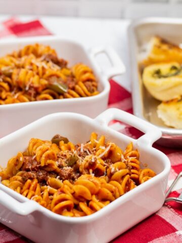 ¾ view of dishes of Instant Pot Tomato Beef Pasta with serving dishes with Parmesan cheese and a tray of garlic bread in the background.