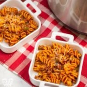 Overhead view of dishes of Instant Pot Tomato Beef Pasta with serving dishes with Parmesan cheese in the background.