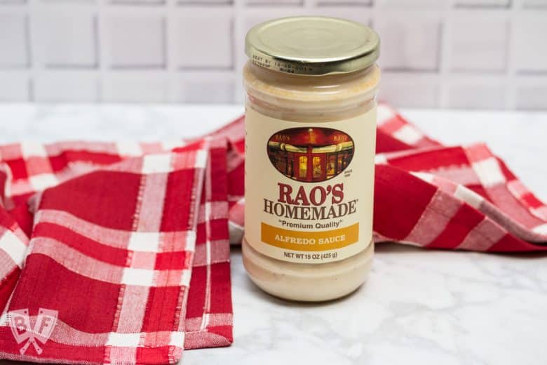 A jar of alfredo sauce in front of a red and white checkered cloth.