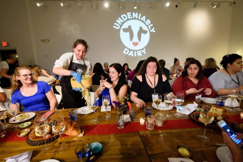 A chef tossing fresh pasta in a cheese wheel for a table full of food bloggers, dairy farmers, and RDNs.