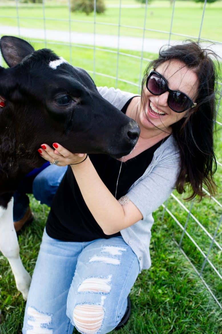 A food blogger snuggling with a baby cow on the farm.