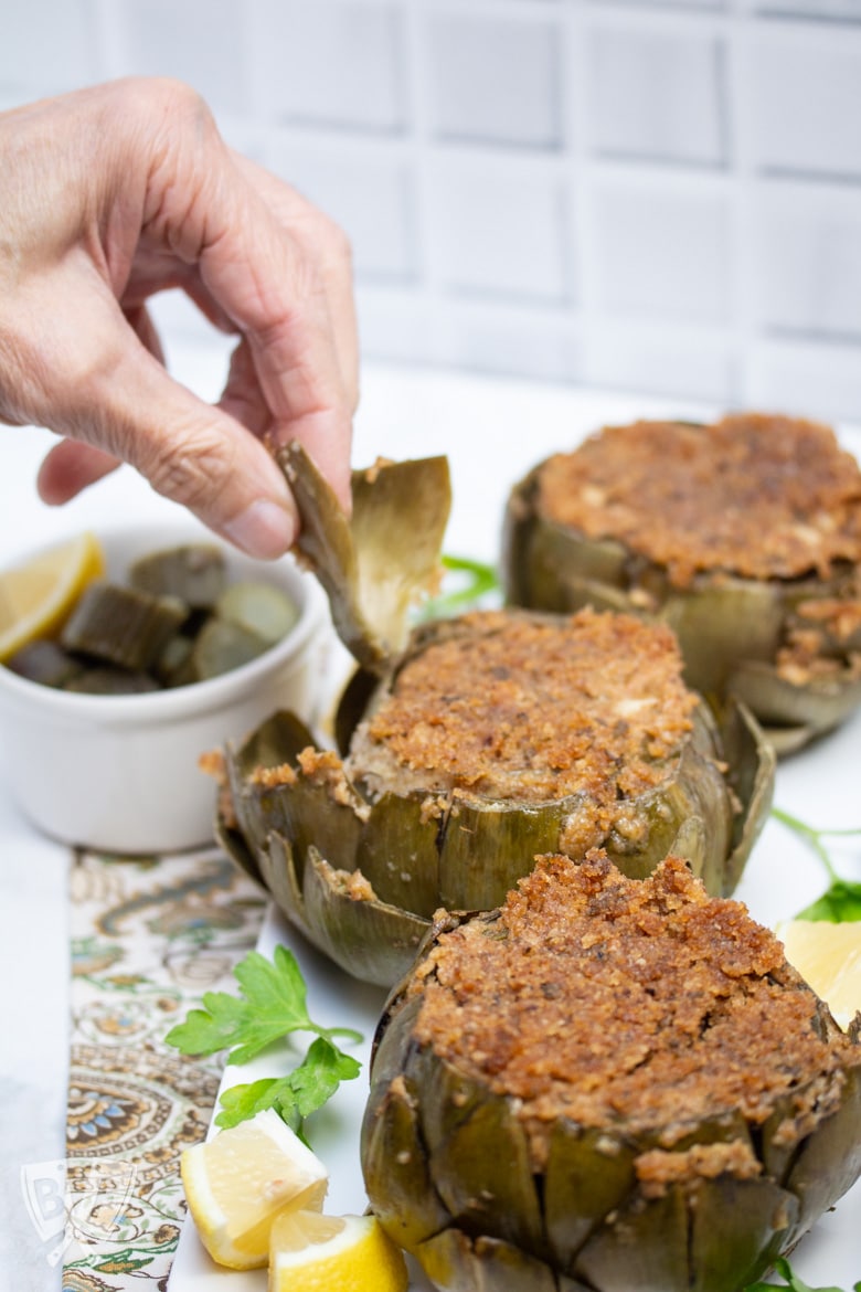 Hand pulling a leaf off of a stuffed artichoke