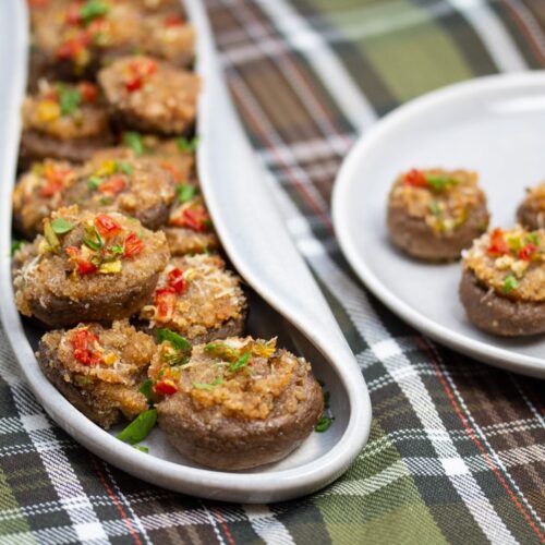 A platter full of Italian stuffed mushroom caps with an appetizer plate alongside..
