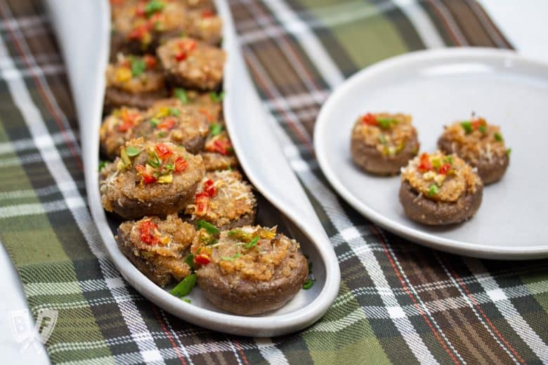 A platter full of Italian stuffed mushroom caps with an appetizer plate alongside..