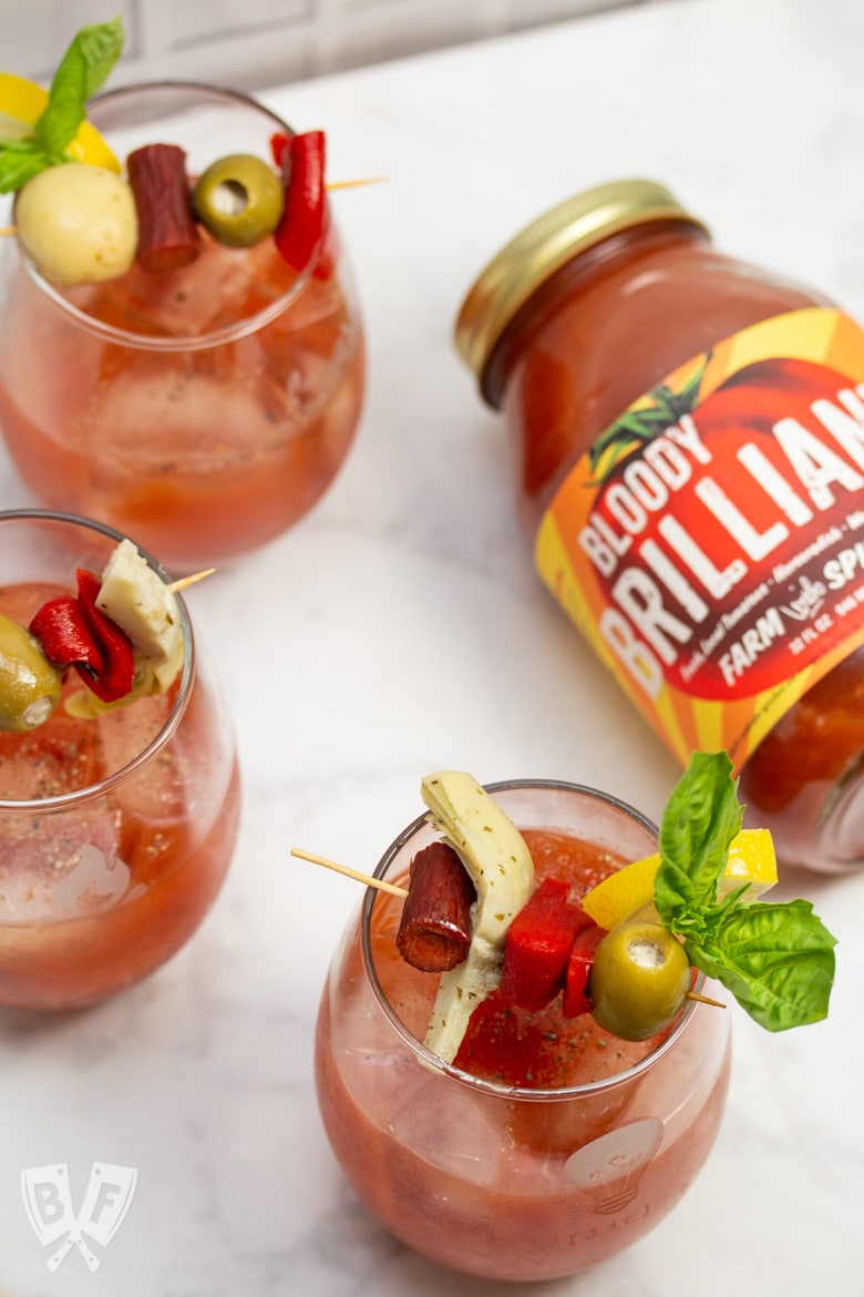 Bloody Mary cocktails garnished with Italian antipasto ingredients next to a jar of Bloody Mary mix.