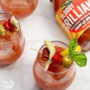 Bloody Mary cocktails garnished with Italian antipasto ingredients next to a jar of Bloody Mary mix.