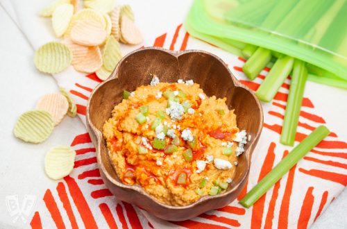 Bowl of buffalo chickpea dip with celery sticks and veggie chips