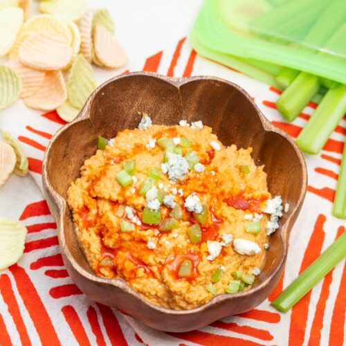Bowl of buffalo chickpea dip with celery sticks and veggie chips
