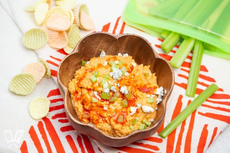 Bowl of buffalo chickpea dip with celery sticks and veggie chips