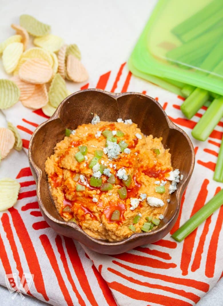 Bowl of buffalo chickpea dips with veggie chips and celery sticks for dipping