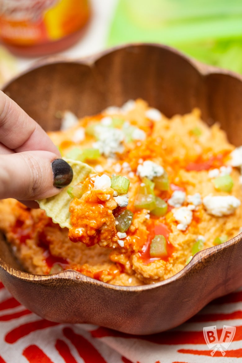 Dipping a veggie chip into a bowl of buffalo chickpea dip