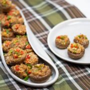 A platter full of Italian stuffed mushroom caps with an appetizer plate alongside..
