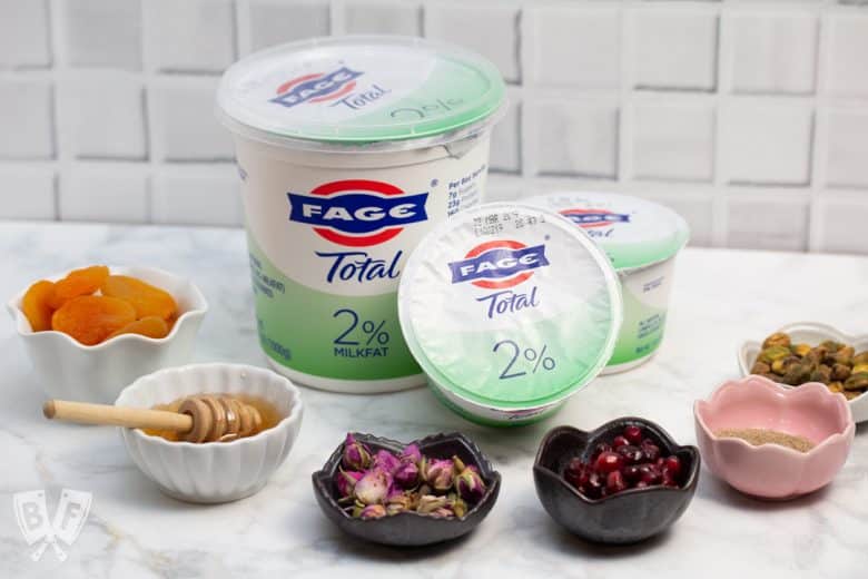 Containers of Greek yogurt surrounded by toppings for Persian Jeweled Yogurt Parfaits.