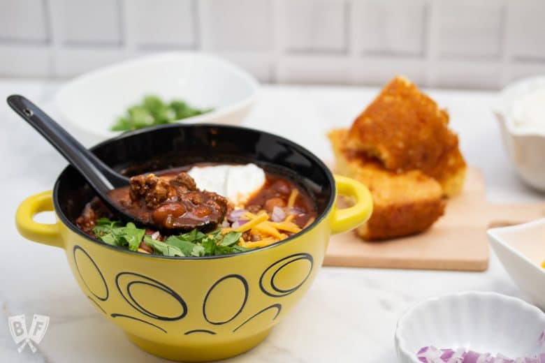 ¾ view of a bowl of Spicy Turkey Three-Bean Chili with toppings and cornbread alongside