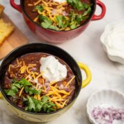 Overhead view of bowls of Spicy Turkey Three-Bean Chili with toppings and cornbread alongside.