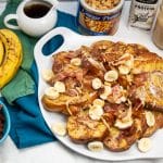 Overhead view of French toast with bananas, bacon, peanut butter, and topping alongside.