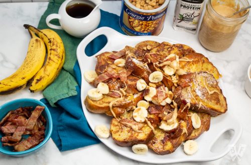 Overhead view of French toast with bananas, bacon, peanut butter, and topping alongside.