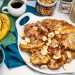 Overhead view of French toast with bananas, bacon, peanut butter, and topping alongside.