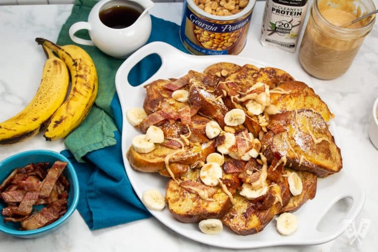 Overhead view of French toast with bananas, bacon, peanut butter, and topping alongside.