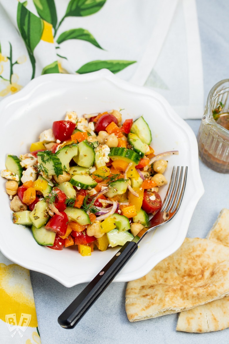 Overhead view of a bowl of Mediterranean Chickpea Salad with Lemon-Herb Vinaigrette with dressing and pita bread on the side