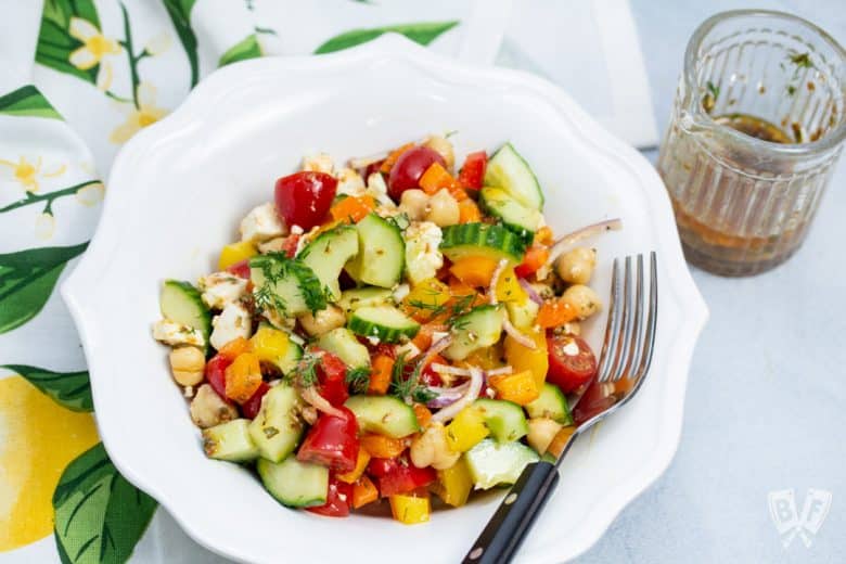 Overhead view of a bowl of Mediterranean Chickpea Salad with Lemon-Herb Vinaigrette with dressing on the side