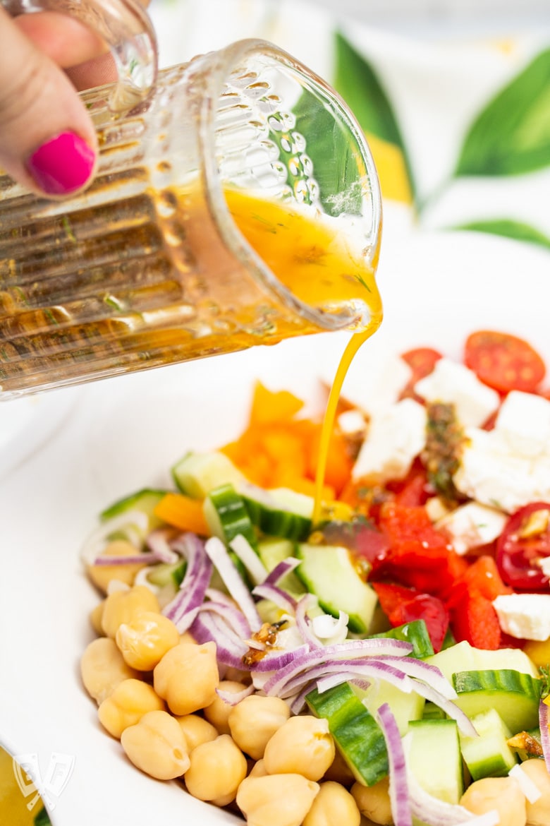 Pouring vinaigrette onto Mediterranean Chickpea Salad with Lemon-Herb Vinaigrette