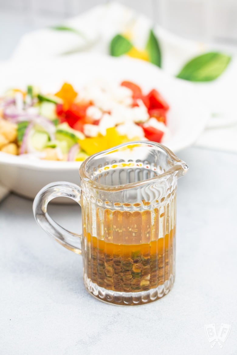 Close-up of a pitcher of lemon-herb vinaigrette with Mediterranean Chickpea Salad in the background