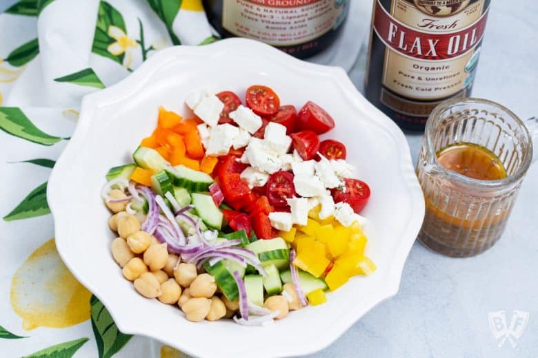 Overhead view of a bowl of Mediterranean Chickpea Salad with Lemon-Herb Vinaigrette with dressing and ingredients to the side