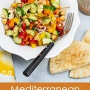 Overhead view of a bowl of Mediterranean Chickpea Salad with Lemon-Herb Vinaigrette with dressing and pita bread on the side