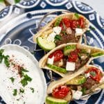 Overhead view of Broiler Kebab served in pita bread with a side of mast-o-khiar yogurt sauce.