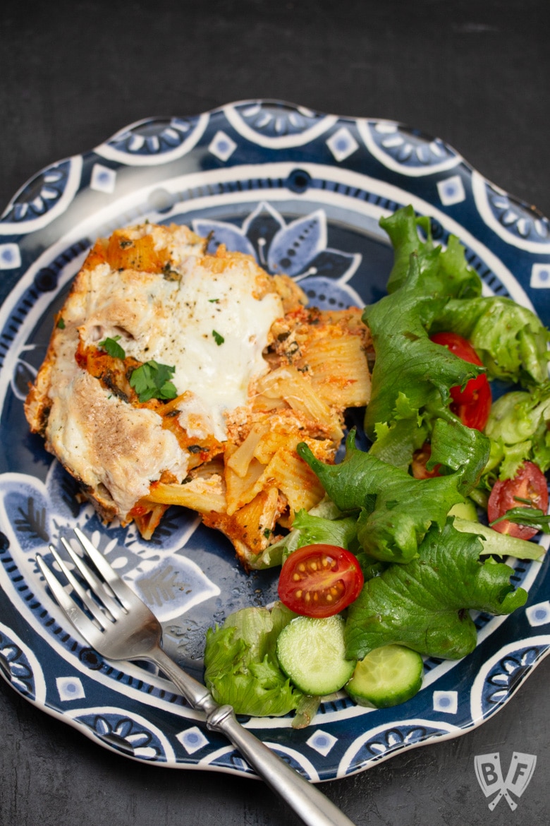 Overhead view of a plate of baked rigatoni casserole with spinach and a salad.