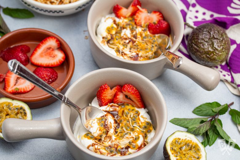 Overhead view of Greek yogurt parfaits with colorful tropical fruit toppings.