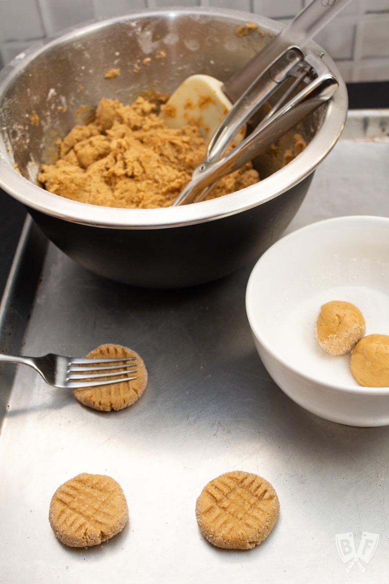 Baking sheet with peanut butter cookie dough and dough balls being pressed with a fork