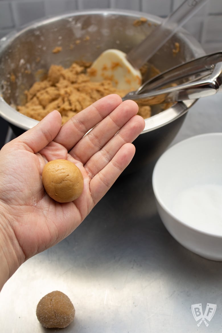 A hand holding a ball of peanut butter cookie dough