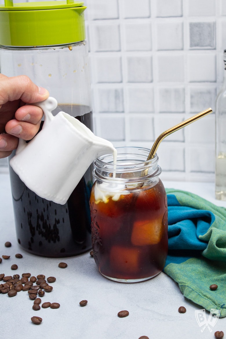 Pouring milk from a pitcher into a glass of homemade cold brew coffee.