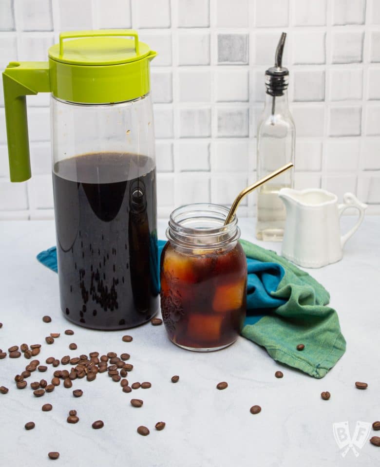 A glass of cold brew coffee along with the pitcher, milk, and sweetener
