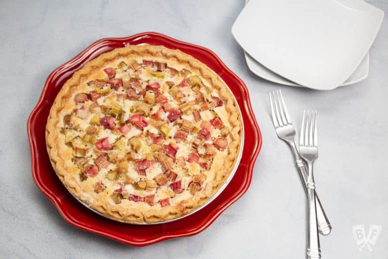 Overhead view of a rhubarb custard pie with forks and plates alongside.