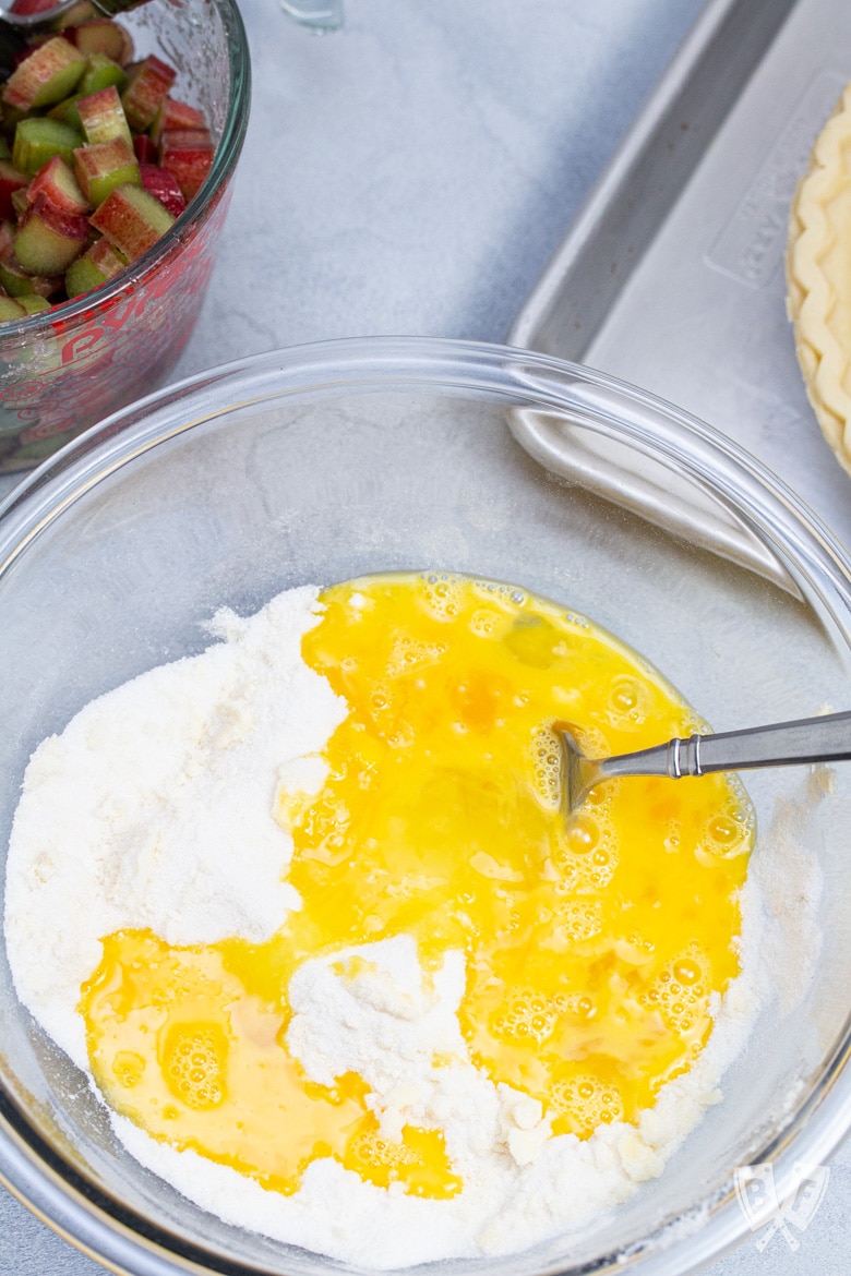 Overhead view of a bowl of custard being mixed for rhubarb custard pie.