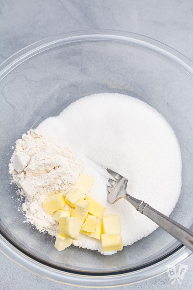 Bowl of sugar with flour, cubes of butter, and a fork.