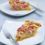 Two slices of rhubarb custard pie on plates with forks.