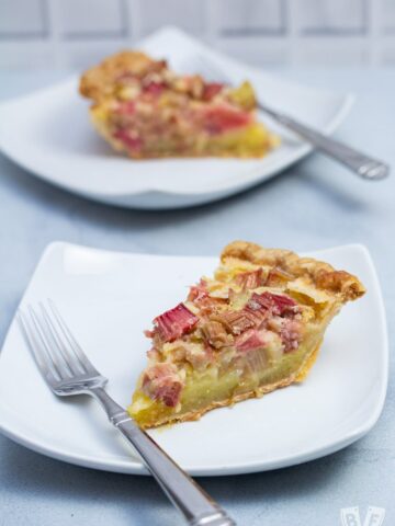 Two slices of rhubarb custard pie on plates with forks.