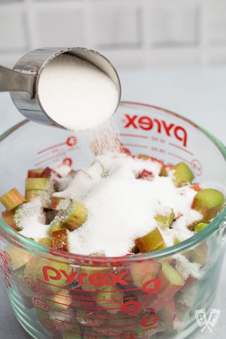 Pouring granulated sugar onto sliced rhubarb.