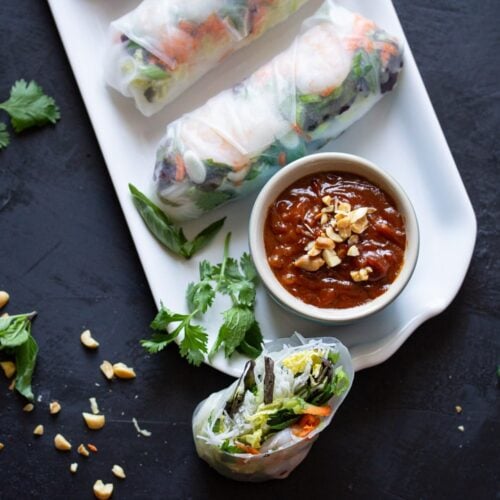 Platter of Vietnamese fresh spring rolls with shrimp & peanut sauce surrounded by ingredients.