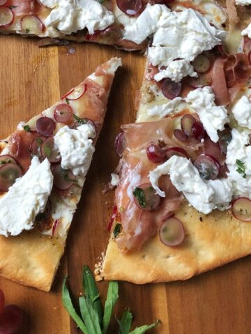 Overhead view of a slice cut out of a Burrata Pizza with Prosciutto and Pickled Grapes