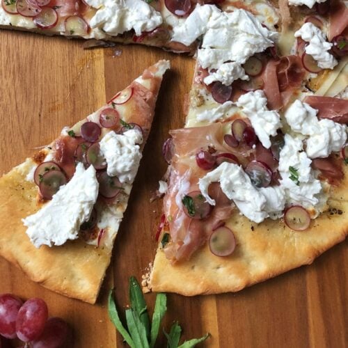 Overhead view of a slice cut out of a Burrata Pizza with Prosciutto and Pickled Grapes