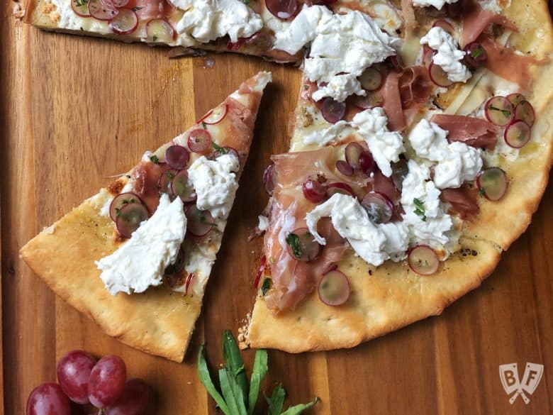 Overhead view of a slice cut out of a Burrata Pizza with Prosciutto and Pickled Grapes