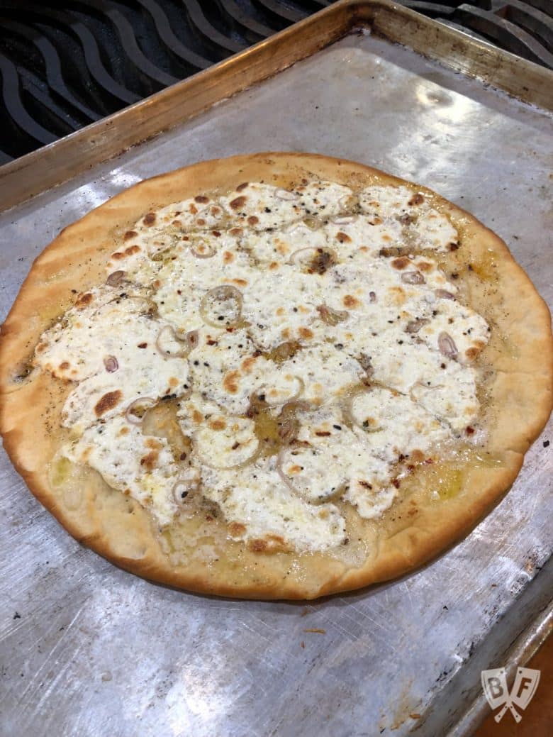 Pizza crust on a baking sheet with melted cheese on top.