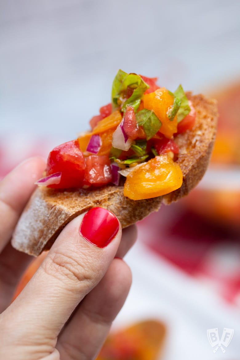 A hand holding a serving of Italian bruschetta