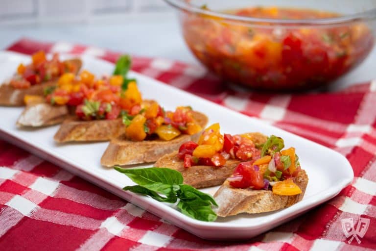 Platter of tomato bruschetta mixture on top of toasted bread with fresh basil.